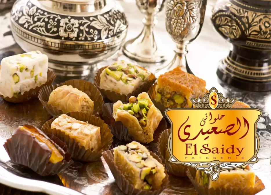 الصورة تحتوي على شعار محلات الصعيدي للحلويات وتعرف على فروع حلواني الصعيدي في مصر حسب كل محافظة في الاسكندرية ودمنهور وكفر الشيخ والمحلة الكبري وأسعار منيو حلواني الصعيدي ورقم الهاتف وخدمة العملاء ومواعيد العمل